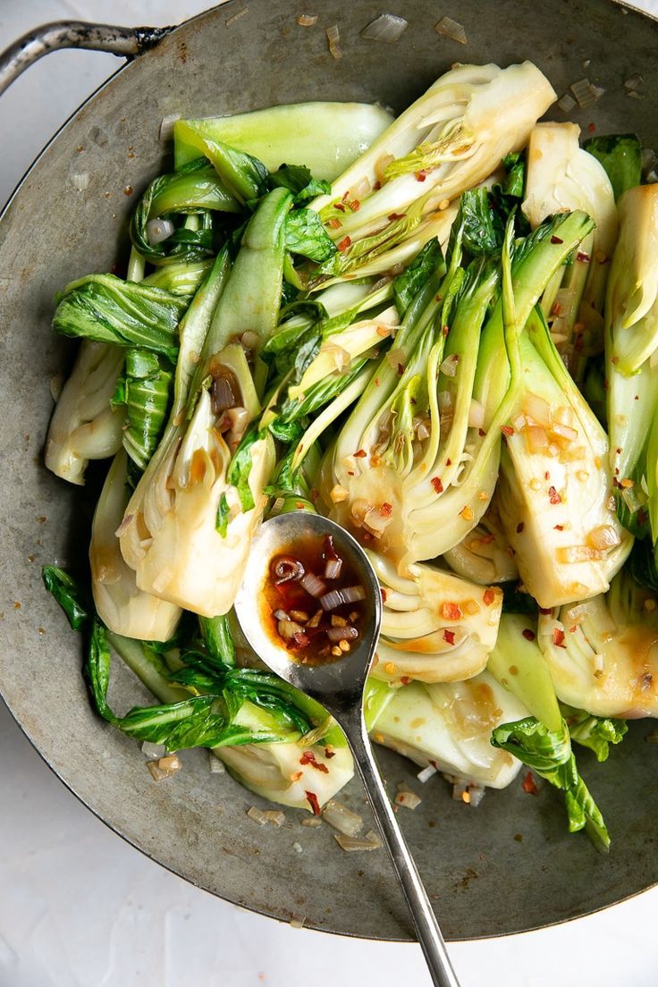 Sauteed baby bok choy fully cooked in an old heavy wok sprin