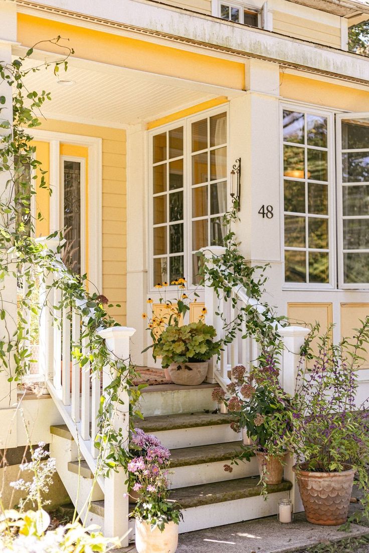Charming yellow house is draped in vines and potted plants a