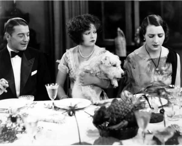 Clara Bow with a dog on her lap during dinner in Hula