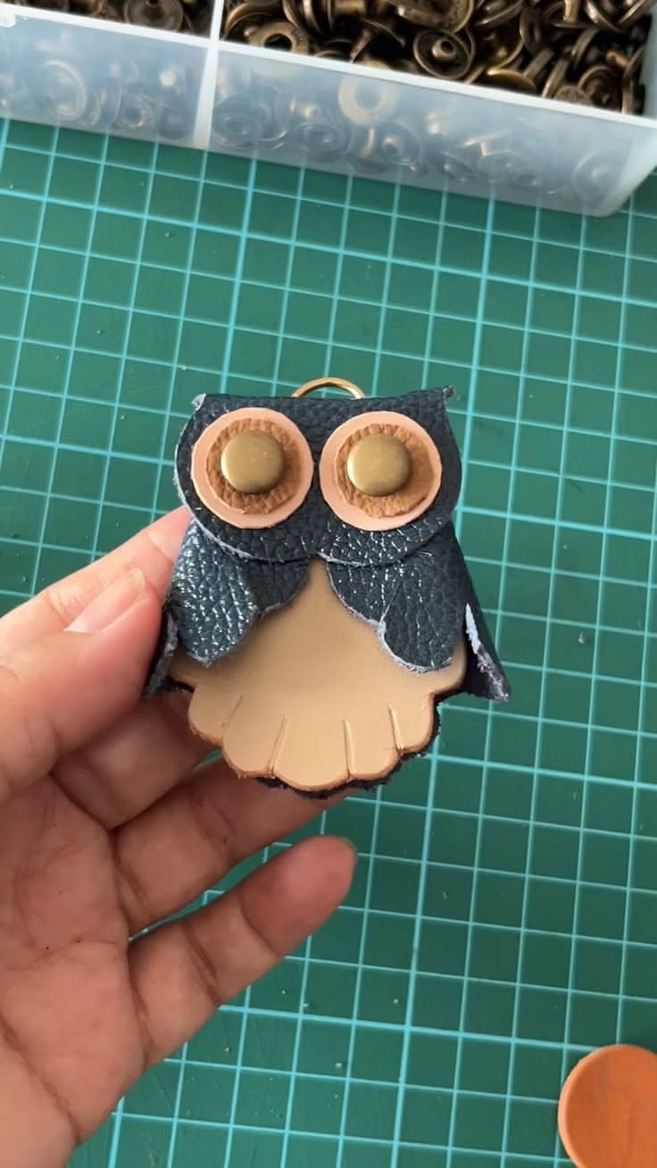 A handmade leather keychain shaped like a cute owl with expr